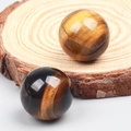 Polished natural tiger eye crystal spheres showcasing golden brown cat-eye texture on wood - Tiger's Eye