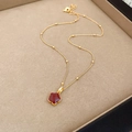 Dettaglio di una collana dorata con ciondolo a fiore in smalto rosso su vassoio beige - Stile Fiore in Smalto Rosso / Oro