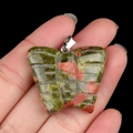 Polished Unakite butterfly pendant with silver bail shown in hand for scale - Unakite