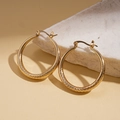 Close-up of golden geometric hoop earrings with spiral texture on white stone - Gold Hoop Earrings / Gold