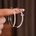 Dettaglio di orecchini a cerchio argento con croce di strass tenuti tra le dita - Argento