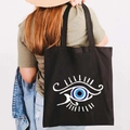 Black canvas tote bag with Greek Evil Eye graffiti print worn on shoulder in casual style - Design G-Classic Totem-Black