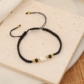 Handmade woven black cord bracelet with white, black and gold beads on natural stone background - Black