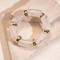 Nahaufnahme eines geometrischen Acryl-Armbands mit goldenen Trennelementen auf Stein - Weiß