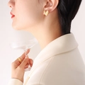 Elegante goldene Herzohrringe und Federring-Set an einem Modell mit einem Glasbecher - Gold