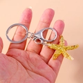 Detail shot of a yellow sequined starfish pendant on a silver keychain held by hand - Yellow Starfish