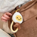 Dettaglio portachiavi a forma di uovo fritto in peluche con sorriso su borsa marrone - Stile Uovo al Tegamino Bianco Giallo