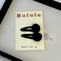 Detail of two black velvet rose hair clips mounted on a branded display card - Black