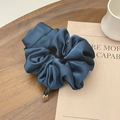 Elegant navy blue satin scrunchie with a gold metal pendant on a wooden tray - Indigo