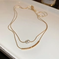 Detailed close-up of double-layer gold necklace featuring a pearl and curved metal bar - Gold