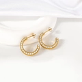 Primer plano de aretes de aro medio dorados con perlas blancas sobre fondo de seda - Dorado