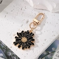 Détail d'un porte-clés fleur de marguerite en émail noir avec des bords dorés - Noir