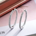 Elegante silberne Creolen mit funkelnden Zirkonia auf weichem rosa-weißem Hintergrund - Ovaler Reif / Silber