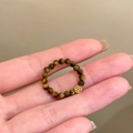 Close-up van tijgeroog kralenring met een gouden muntbedeltje op een warme basis - Bruine Kralen Munt Stijl