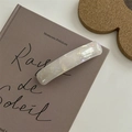 Fermaglio per capelli in resina bianca iridescente su un libro con luce naturale - Clip a molla