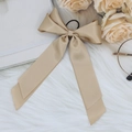 Detailed view of beige satin ribbon bow hair tie with elastic band on soft white fabric - Khaki
