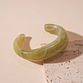 Macro detail of olive green marble acrylic cuff bracelet resting on stone texture - Marbled Green Open Bangle