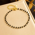 Bracciale boho dorato con perline sfaccettate nere posato su una scatola regalo oro - Bracciale (B1405)
