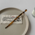 Detail of tortoise shell acetate hair pin with spiral twist design on ceramic tray - Caramel color