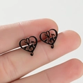 Detail of black heart-shaped music note earrings in stainless steel on hand - Black