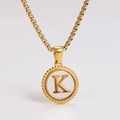 Macro detail of golden letter K pendant with pearl shell inlay and beaded circular edge - Letter K