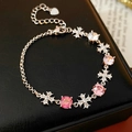 Detail eines Zirkon-Kreuzarmbands mit rosa Steinen auf einer schwarzen Lederbox - Silber-Rosa
