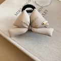 Detail of beige bow hair claw clip with golden metal tag on soft padded fabric - Beige