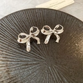 Détail de boucles d'oreilles nœud argenté avec éclat métallique sur socle texturé - Nœud Papillon d'Argent (Tige en Acier Inoxydable)