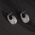 Minimalist silver steel hoop earrings with streamlined wave texture on black background - Silver