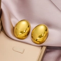 Macro shot of gold oval stud earrings with polished mirror finish on champagne silk - Gold