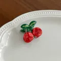 Détail d'une jolie pince à cheveux cerise rouge posée sur une assiette en céramique - Cerise