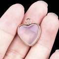 Pink heart-shaped quartz pendant with gold plated metal border held by fingers - Synthetic Opal Gold Edging