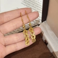 Eleganti orecchini a nappa dorati con cerchi traforati tenuti in mano in un set caldo - Stile a Gancio / Oro