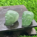 Green crystal skulls carved from natural stone on a moist wooden base with garden background - Green Aventurine
