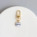 Close-up of a golden metal keychain with a cute grey and white enamel cat charm pendant - Grey Cat