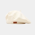 Détail d'un béret en maille avec étiquette en cuir marron et texte 'LOVE STYLE' - crème
