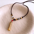 Detail of golden cylinder pendant with engraved scriptures and multi-color beaded rope - Gold