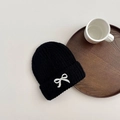 Detail shot of black knitted beanie featuring delicate white embroidered bow decoration - 3-8 Years / Black