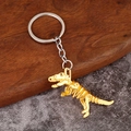 Makroaufnahme eines goldenen T-Rex-Skelett Schlüsselanhängers auf rustikalem Holzhintergrund - Matt Gold T-Rex Skelett