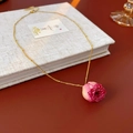 Détail d'un collier chaîne dorée avec un pendentif bouton de rose rose éternelle sur un livre - Collier - Or - Violet