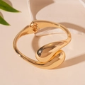 Primer plano de brazalete abierto de gota dorada con textura metálica sobre piedra - Brazalete Abierto Gota / Dorado