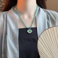 Detail of emerald green beaded necklace with floral pendant on a silk fabric background - Style 13 Necklace - Green Safety Lock