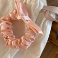 Close-up of a pink satin bow scrunchie with pleated texture and ivory drawstring bag - Pink