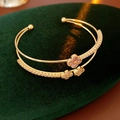 Close-up of double-layer gold bangle with cubic zirconia clover charms and open design - Gold-Pink