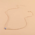 Dettaglio della collana a catena O dorata con ciondolo occhio blu su sfondo rosa tenue - Oro