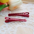 Close-up of red electroplated metal hair clips with wavy edges on white floral lace - Burgundy
