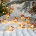 Christmas LED bell string lights with red bows and warm glow on white plush surface - Bell