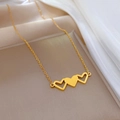Dettaglio macro della collana in acciaio al titanio dorato con tre ciondoli a cuore - Stile a Tre Cuori Collegati (M205 Oro) / Oro