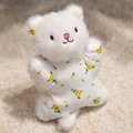 Cute white plush bear toy wearing yellow floral clothing in a cozy setting - White Cat