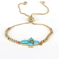 Detailed macro view of gold-plated box chain bracelet with blue zircon cross charm - Turquoise Blue